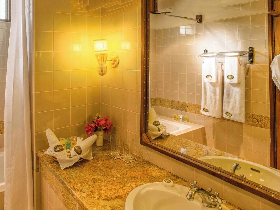 A bathroom with a bathtub, sink, and mirror. There are towels and toiletries on the counter.