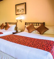 Habitación de hotel con dos camas, cada una con una colcha estampada, una mesita de noche, una lámpara y un cuadro en la pared.