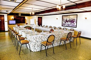 Un salón de conferencias con una larga mesa, sillas, una pantalla de proyector y una fotografía histórica enmarcada en la pared.