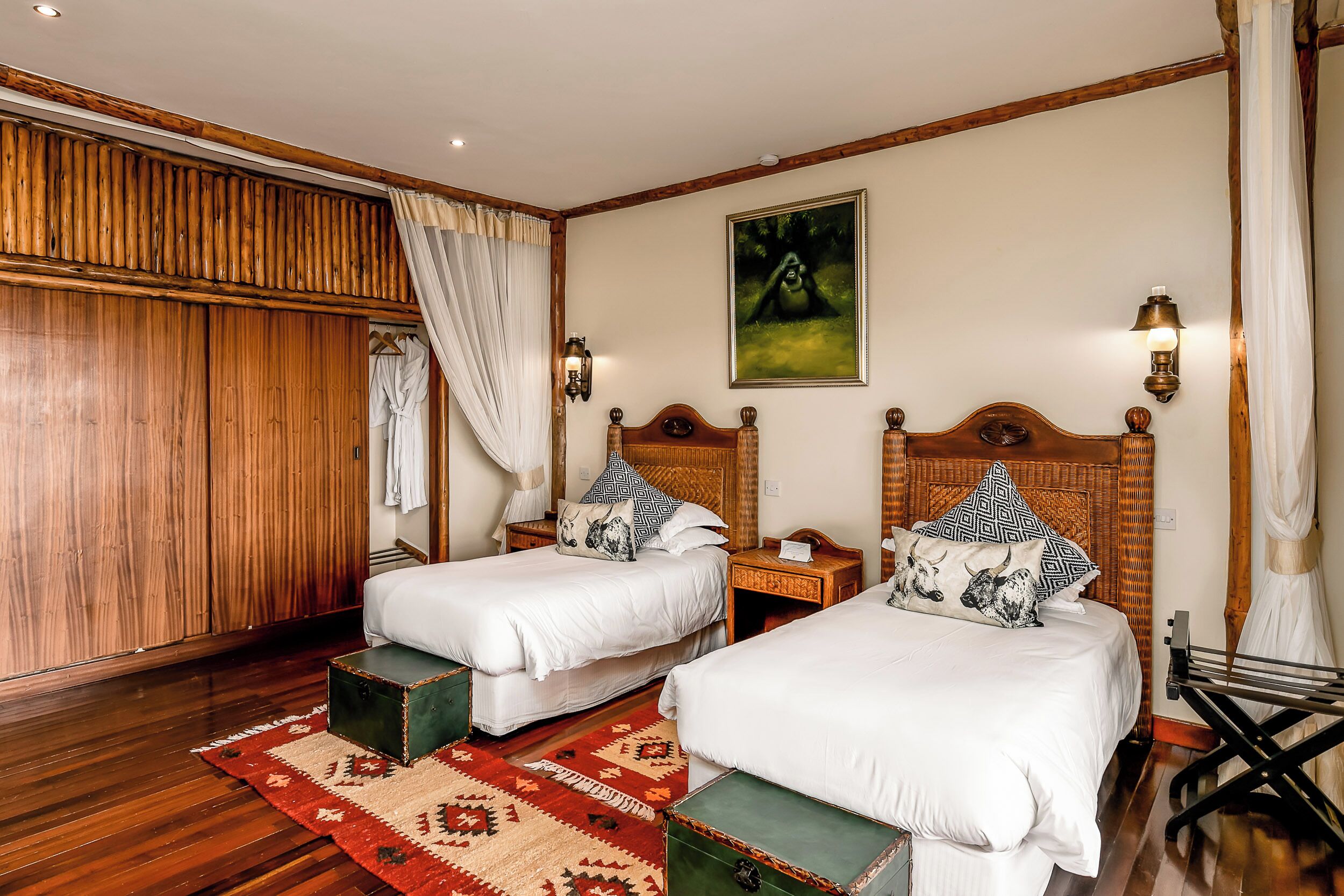 A hotel room with two single beds, wooden headboards, a large mirror, a wooden wardrobe, and a red patterned rug.