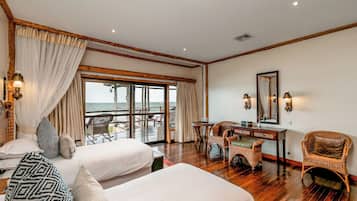 Une chambre d’hôtel avec deux lits, un bureau, des fauteuils en osier, une grande fenêtre donnant sur un beau paysage et un balcon.