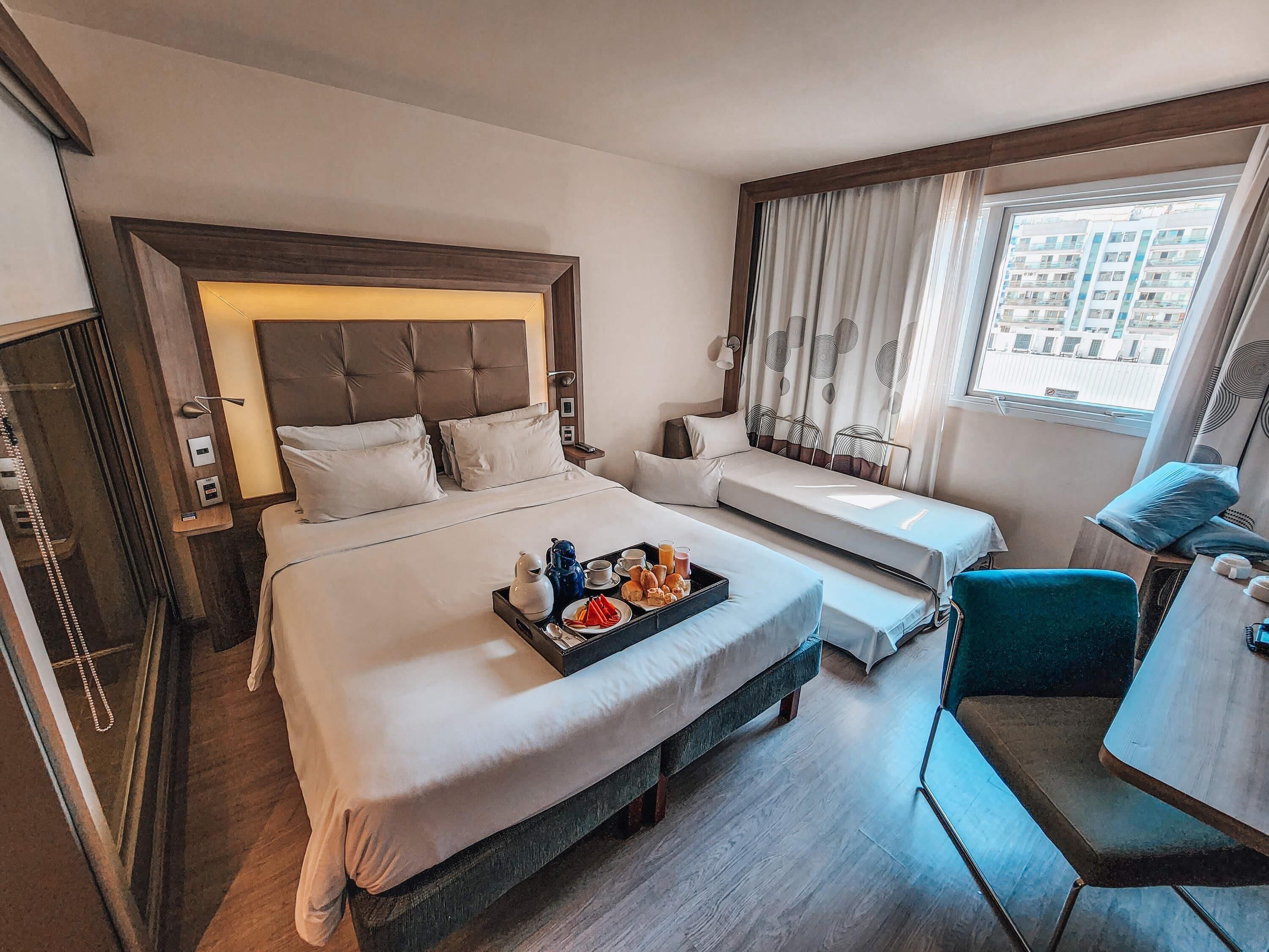 A hotel room with two beds, a desk, and a window with curtains.