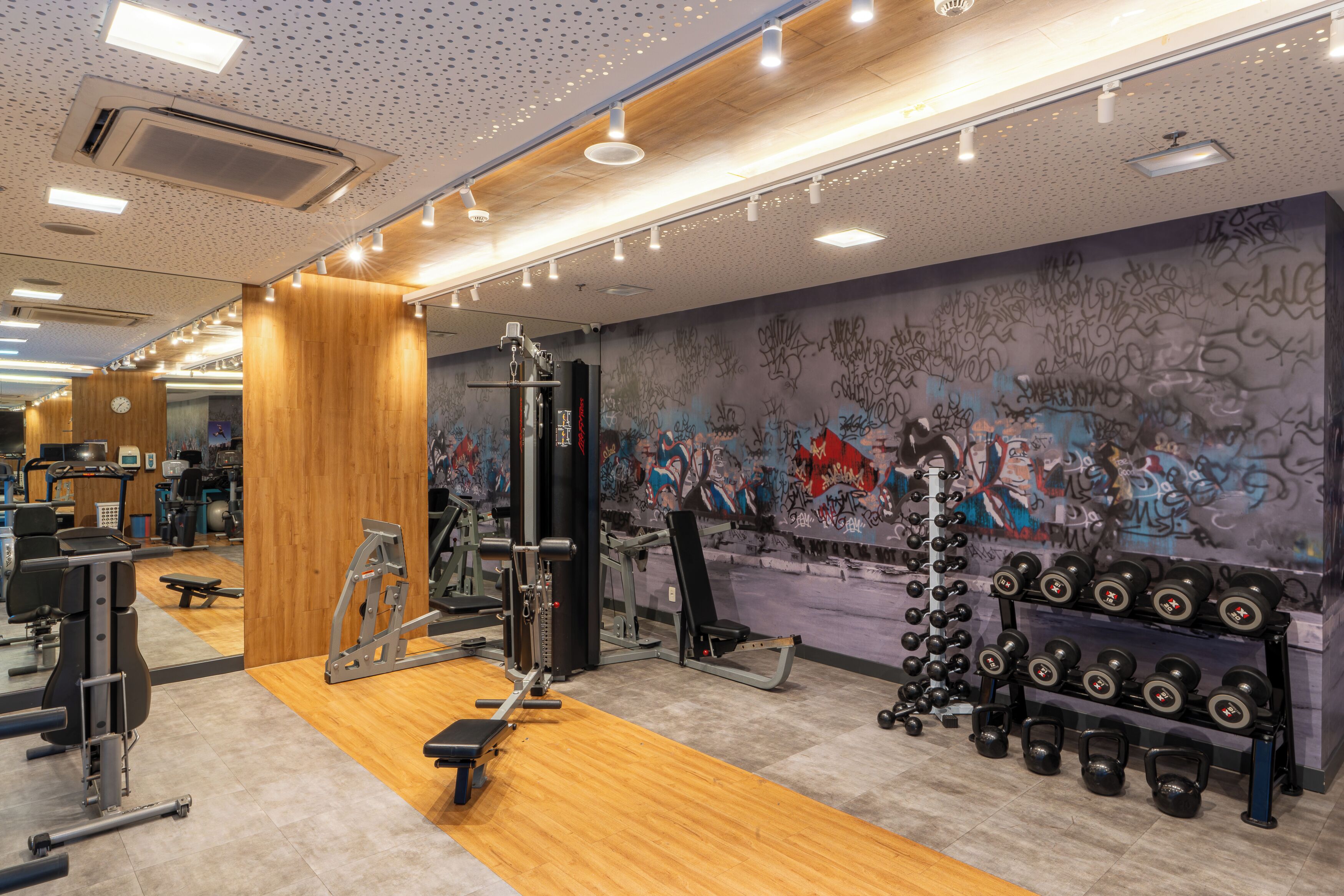 A gym with various exercise equipment, a wooden floor, and a graffiti-covered wall.