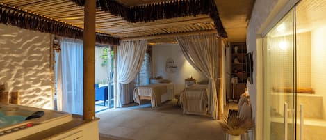 A room with a bed, a small table, a chair, and a glass shower area.