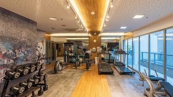 Uma academia com equipamentos de exercício, piso de madeira e grandes janelas.