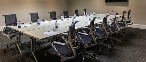 A conference room with a long table, chairs, water bottles, and a flat-screen TV on the wall.