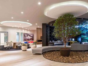 A modern interior with a curved seating area, a large tree, and a wall with a nature-themed mural. - Novotel RJ Praia de Botafogo Hotel (Rio de Janeiro)