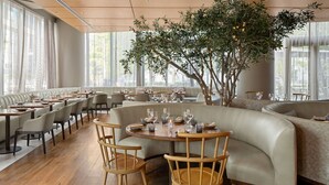 Un restaurante moderno con una zona de estar curva, sillas de madera y un árbol central con luces.