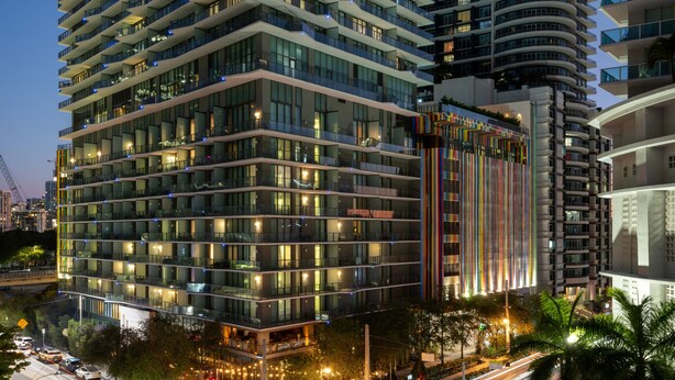 Un moderno edificio de gran altura con varios balcones y ventanas amplias, rodeado por una calle urbana bien iluminada.