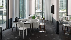 Habitación de hotel moderna con un ventanal grande, un sofá, una mesa de centro, un televisor y un balcón con vista a la ciudad.