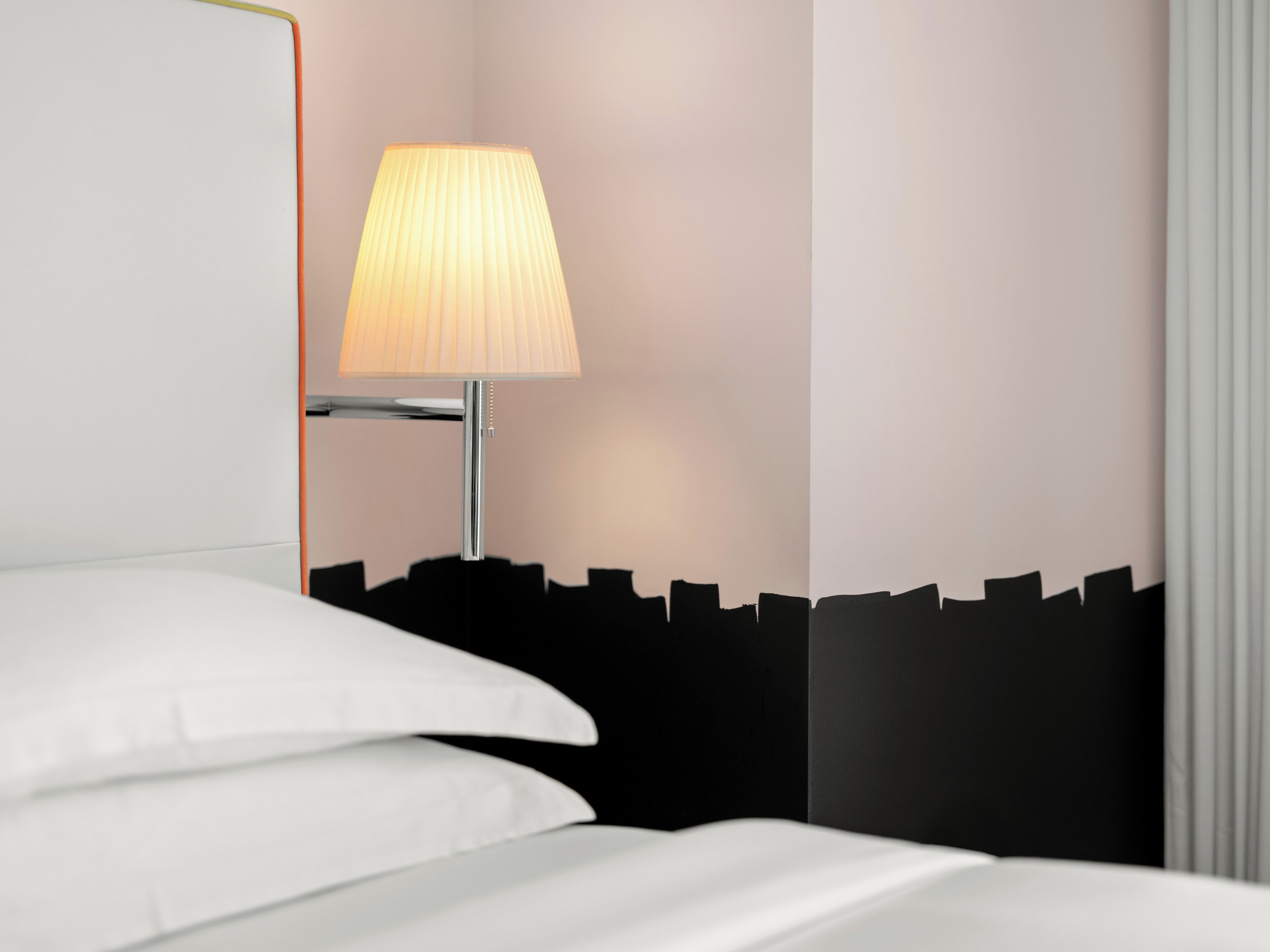Una cama bien hecha con ropa blanca, una lámpara moderna con pantalla acanalada y un papel tapiz blanco y negro.