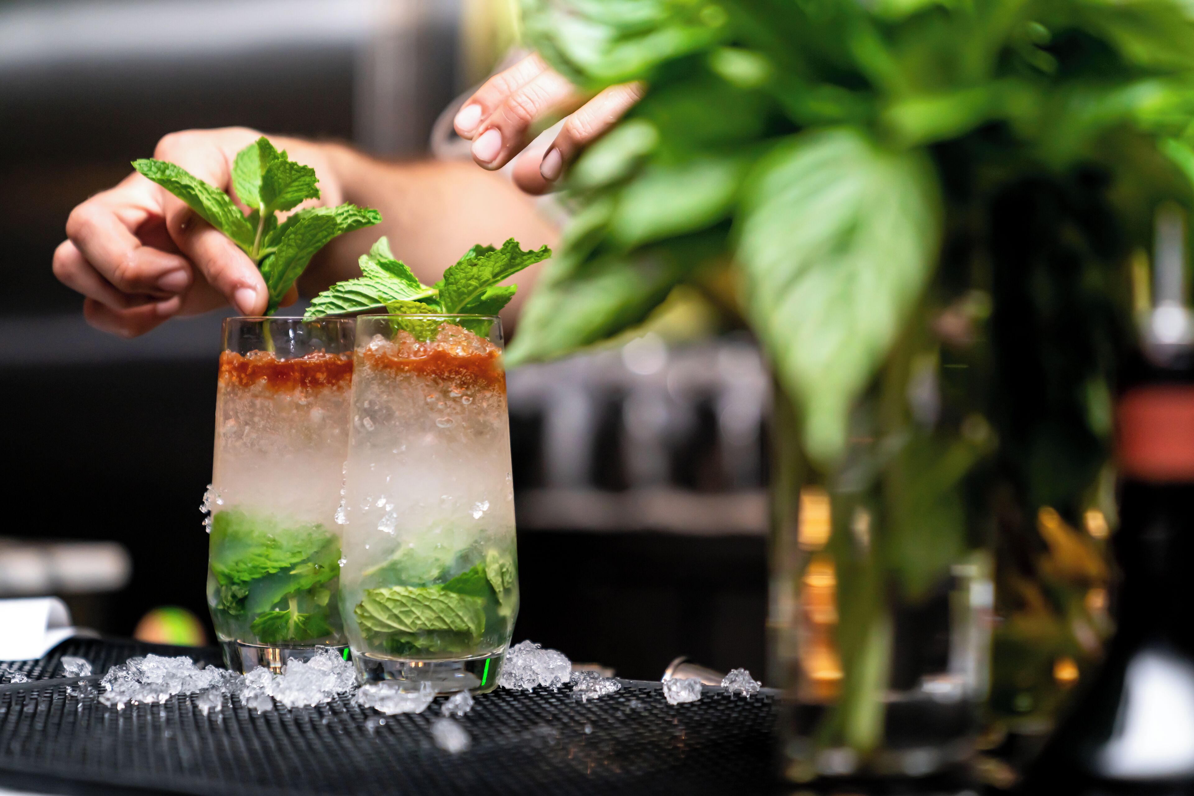Dos vasos de una bebida adornada con hojas de menta, sobre una bandeja con cubitos de hielo.
