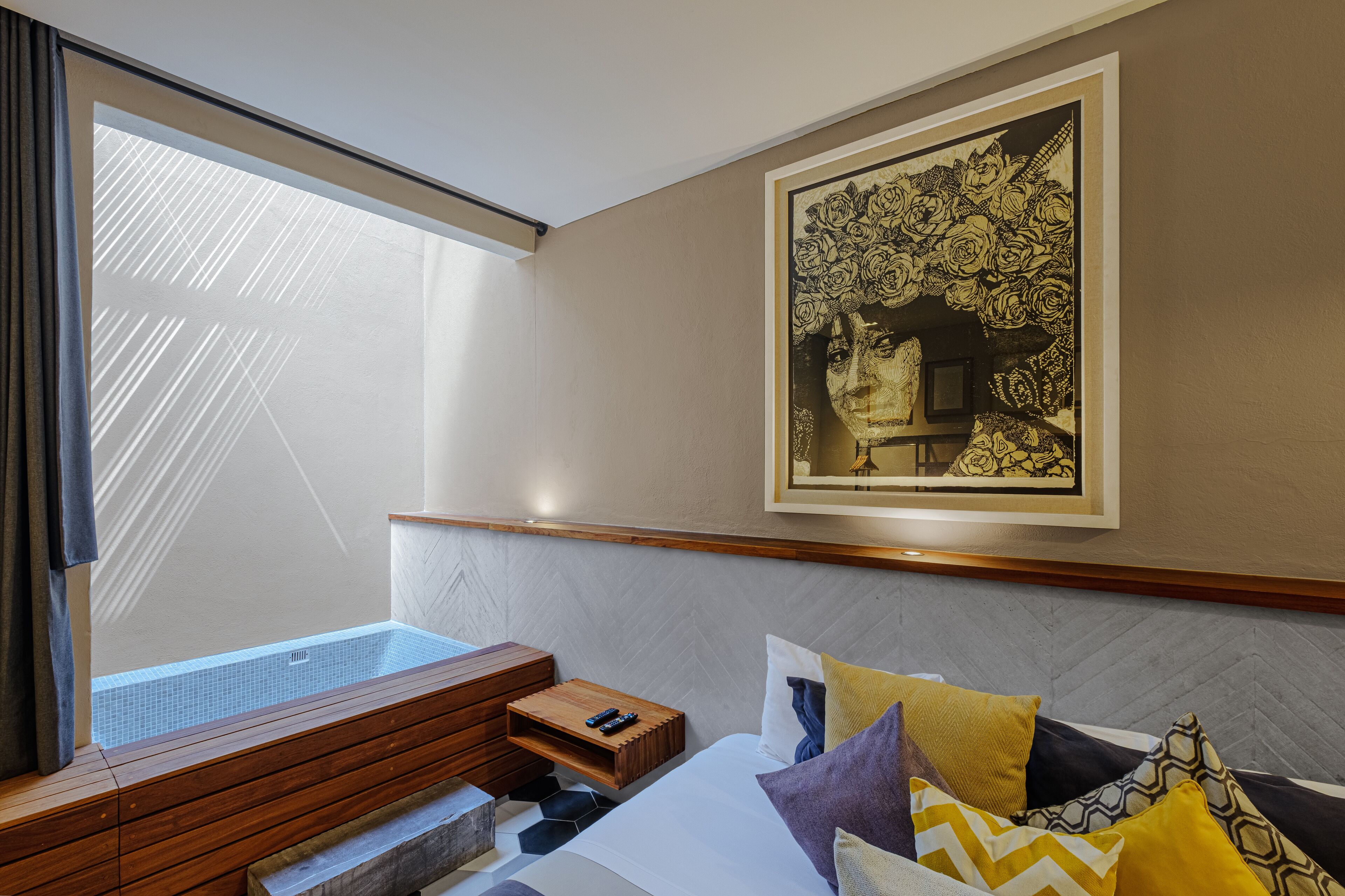 Une chambre d’hôtel avec un lit, un banc en bois, une petite table et une grande fenêtre.