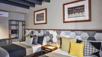 A modern hotel room with a bed, bedside tables, a desk, and a chair. There are two framed artworks on the wall.