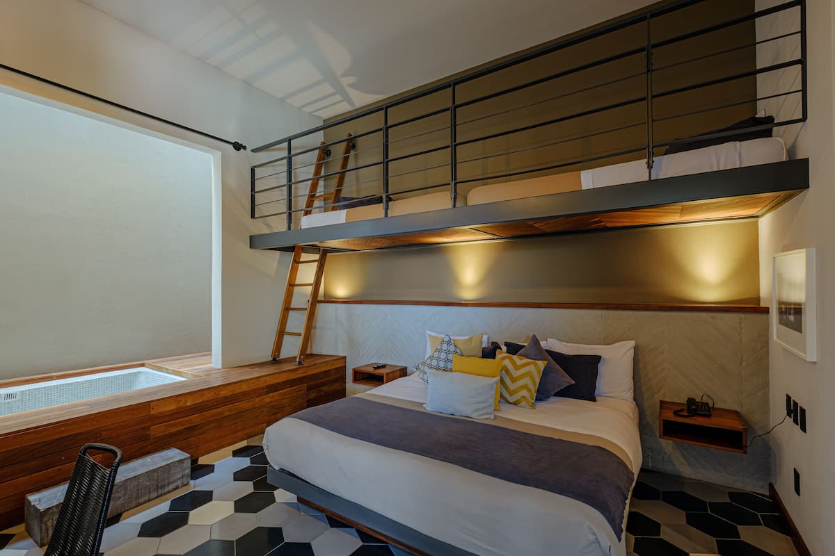 A modern bedroom with a bunk bed, a wooden bench, a ladder, a bedside table, and a small shelf.