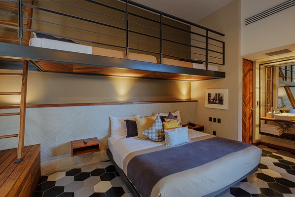 A hotel room with a bunk bed, a wooden headboard, a bedside table, and a bathroom with a mirror and sink. - Hotel Criol (Querétaro)
