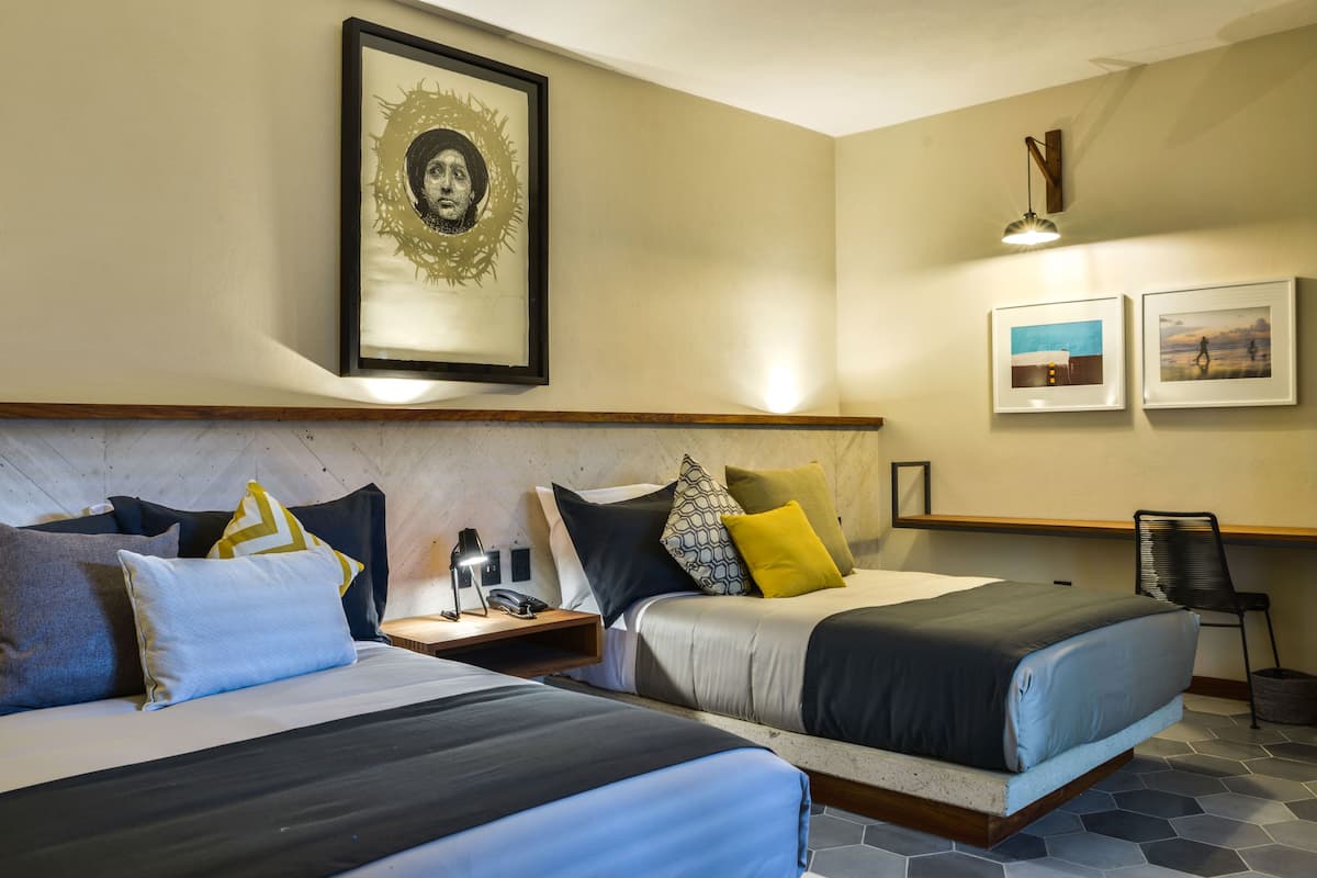 A hotel room with two beds, a nightstand, a lamp, a framed picture on the wall, and a chair.