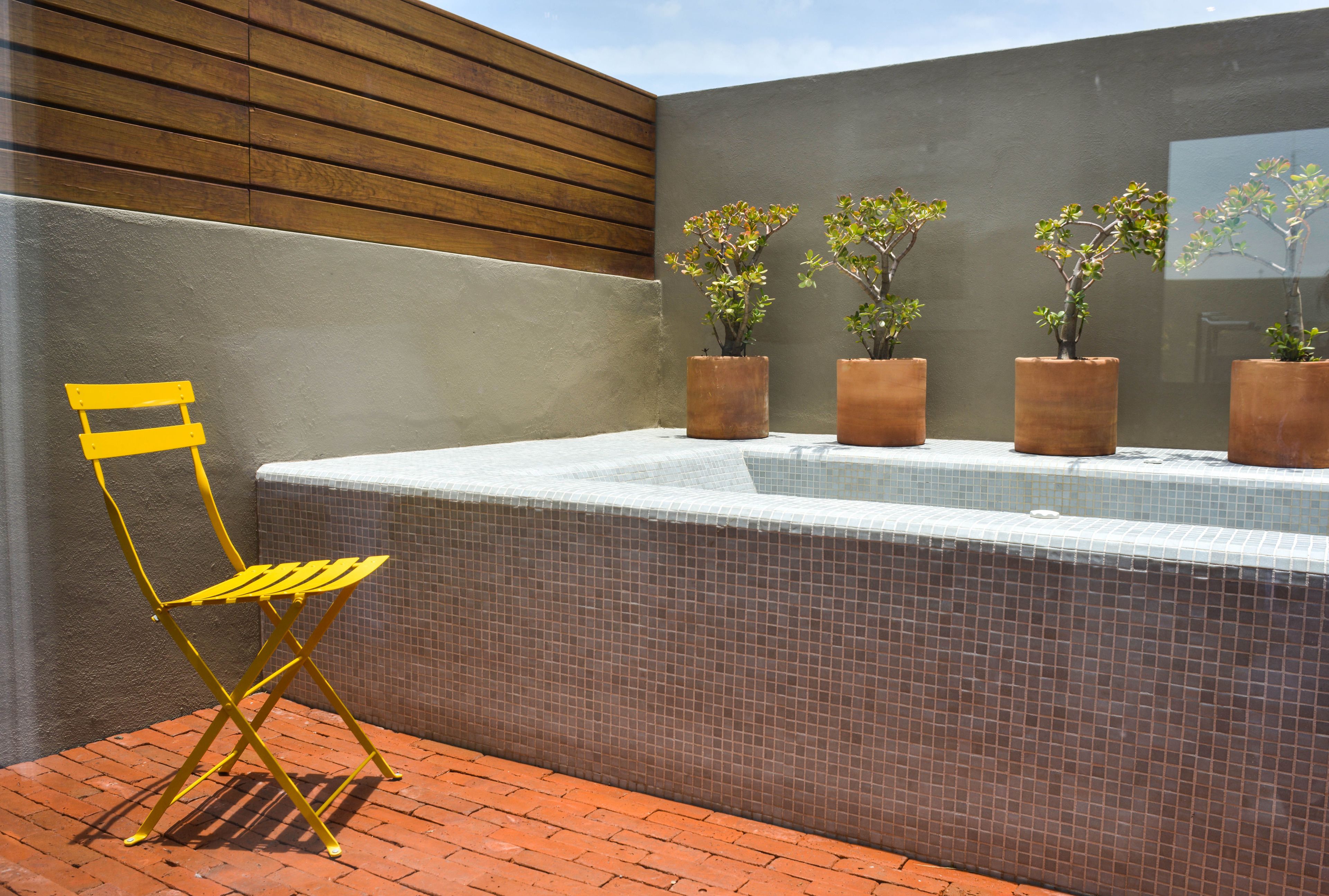 Een terras met een terrastegelvloer, een gele klapstoel en een rij potplanten tegen een muur met houten panelen en betegelde delen.