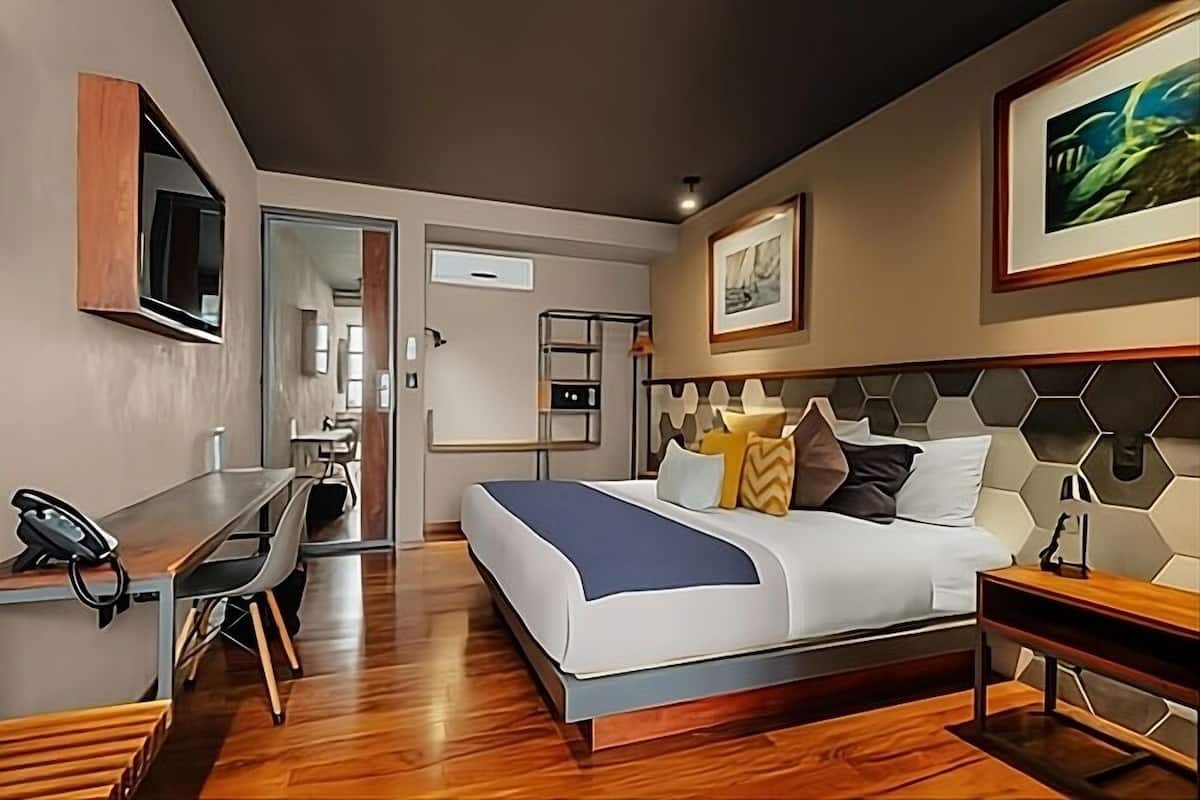 A modern hotel room with a bed, desk, and a view of the hallway.