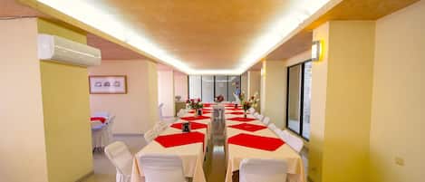 Una sala conferenze con lunghe tavole, sedie bianche e tovaglioli rossi.