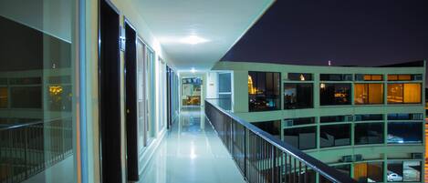 A long, narrow corridor with glass doors on one side and a railing on the other, leading to a lower level.