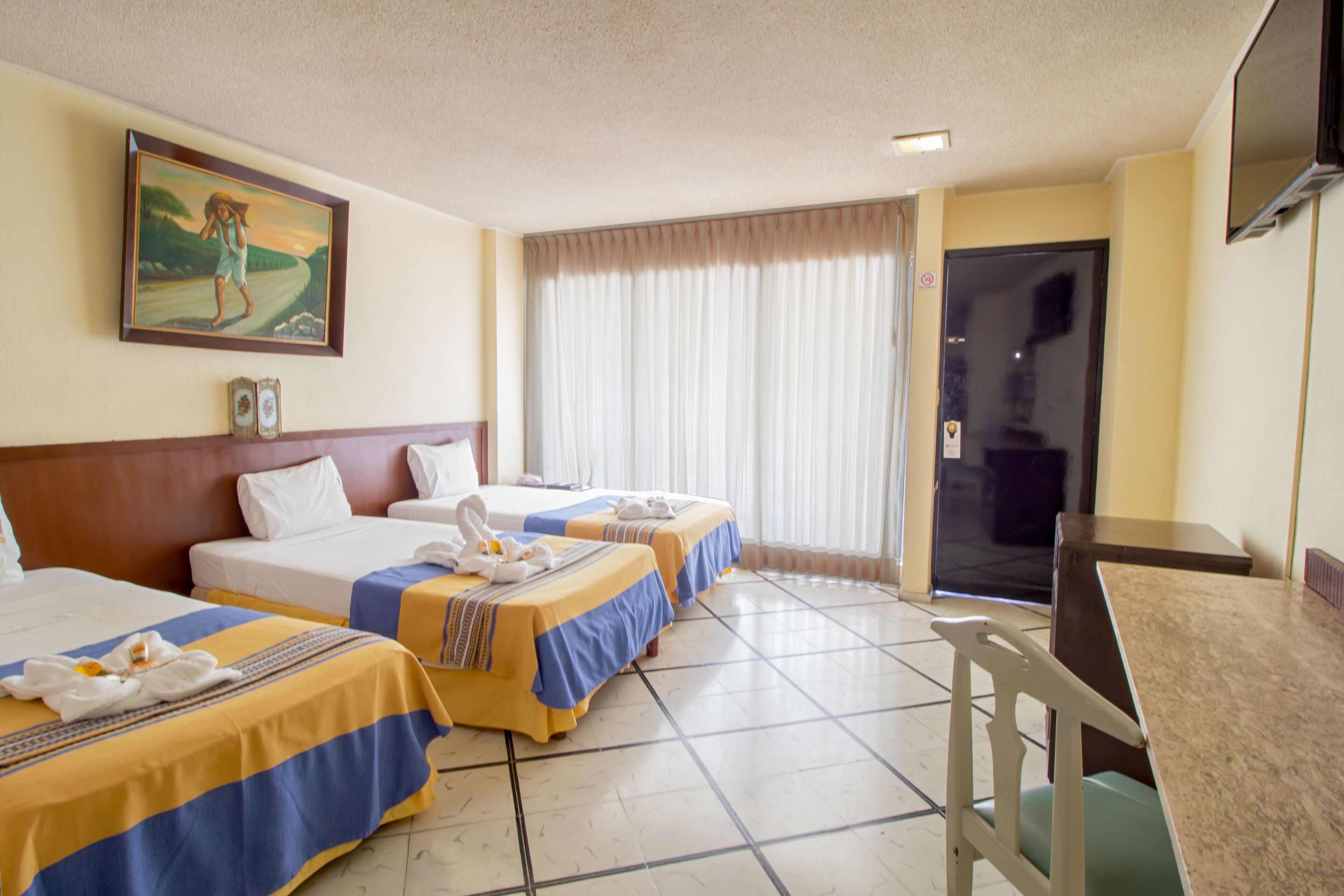 A hotel room with two beds, a dining table, a TV, and a painting on the wall.