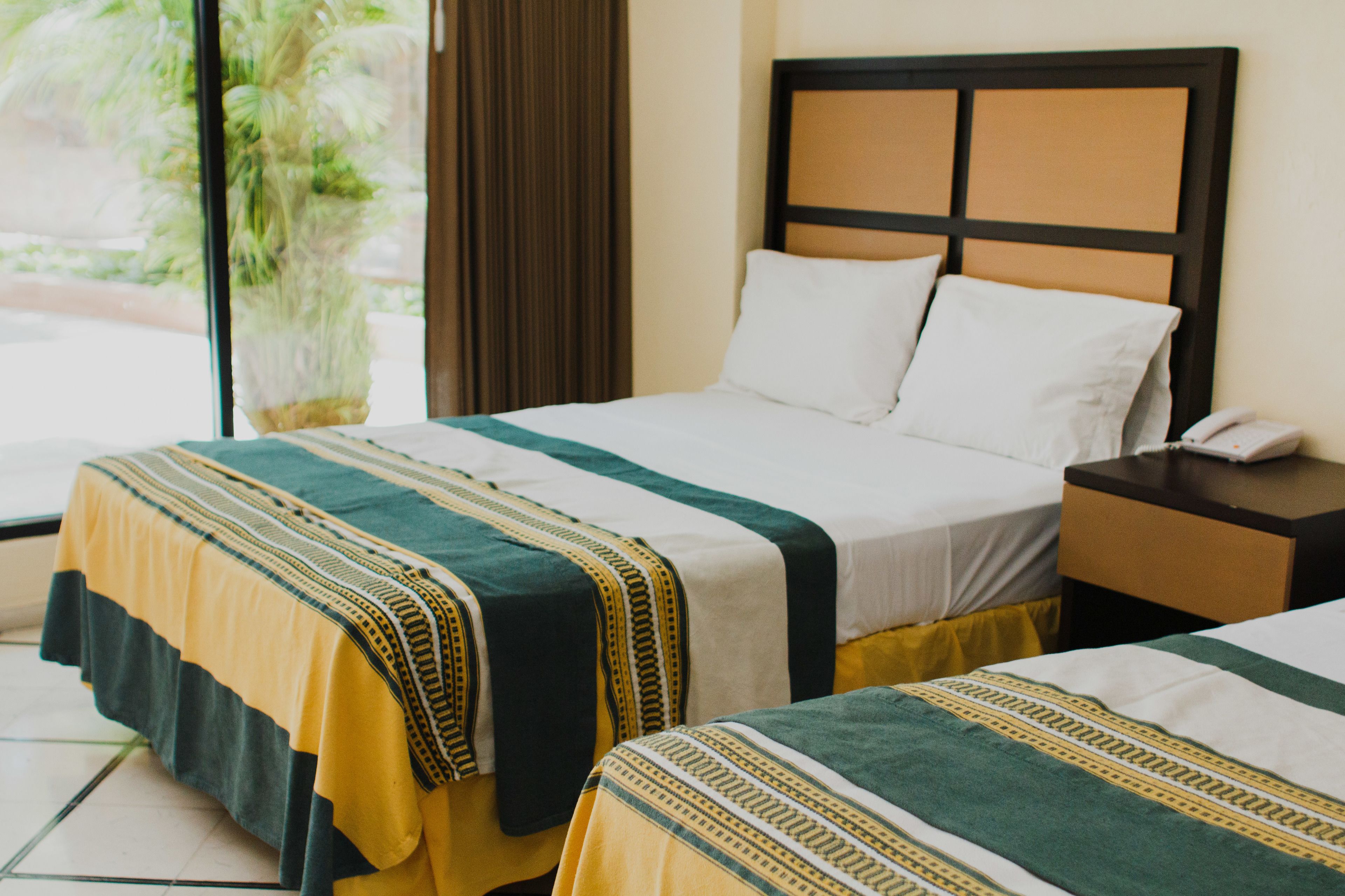 A hotel room with two beds, each with a striped bedspread, a nightstand with a phone, and a window with curtains.