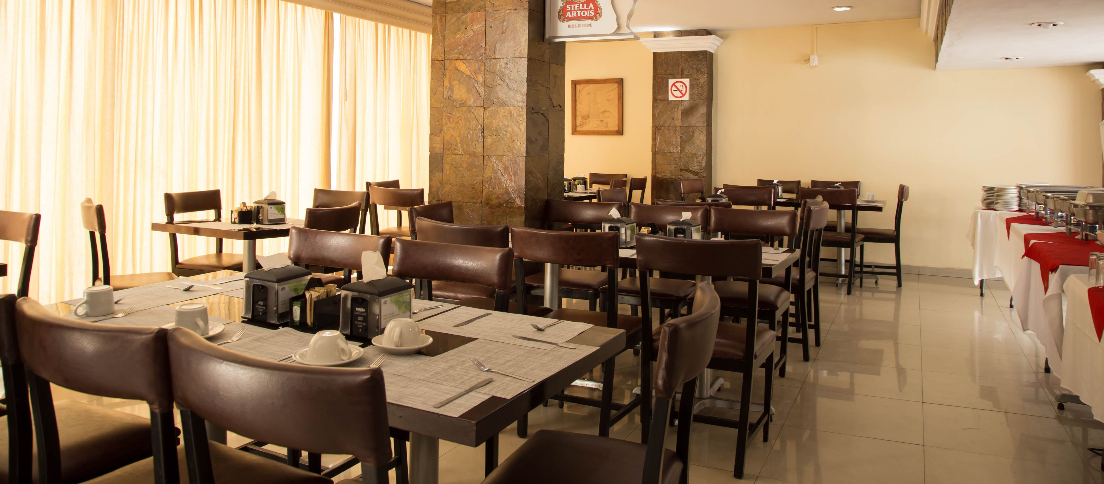 A restaurant with multiple tables and chairs, a stone wall, and a sign indicating no outside food.