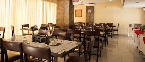 A restaurant with multiple tables and chairs, a stone wall, and a sign indicating no outside food.