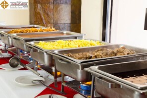 A buffet setup with various food options, including rice, meat, and other dishes, arranged on stainless steel serving trays.