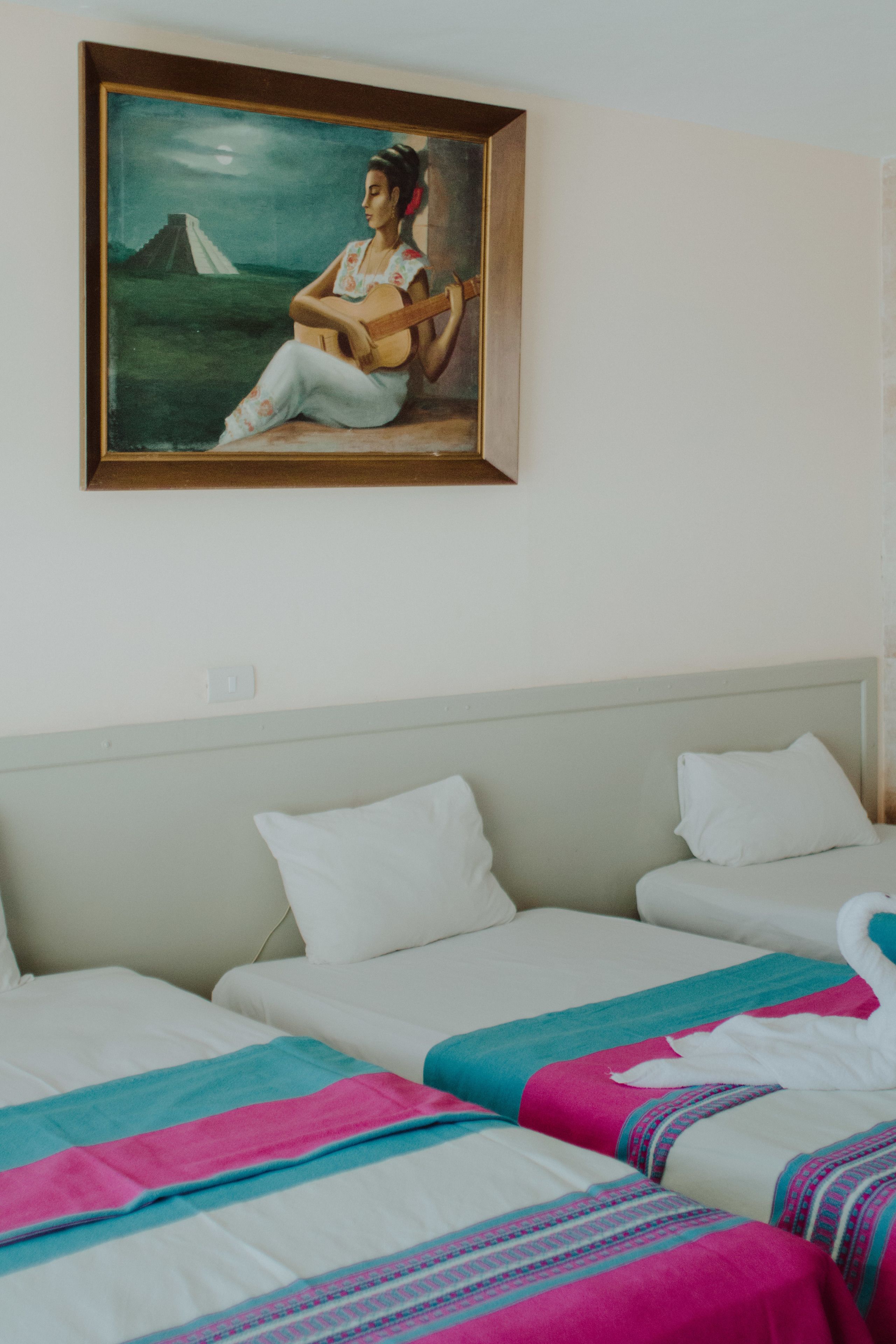 A hotel room with two beds, a painting of a woman playing guitar, and a view of a mountain.