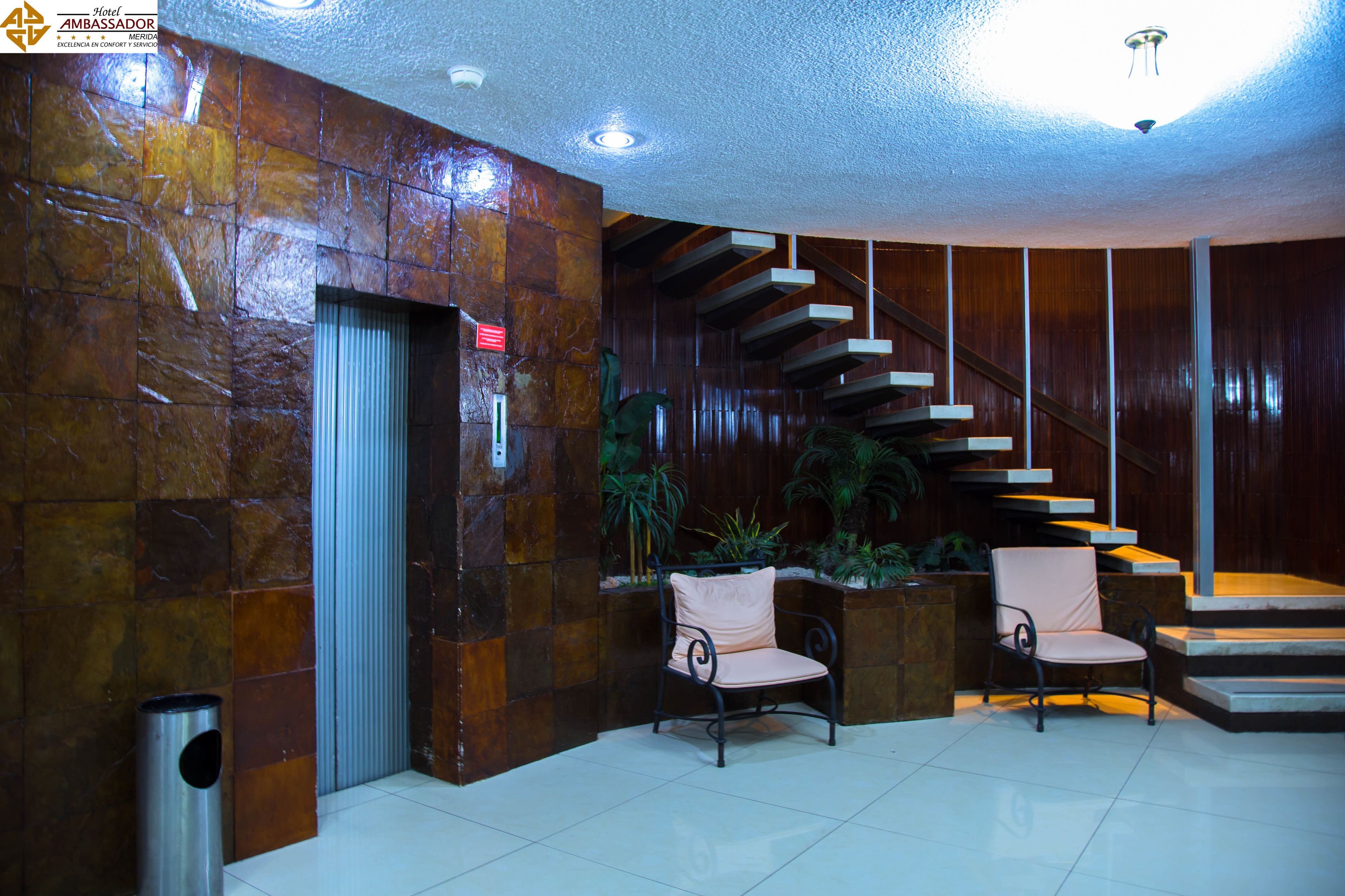 A lobby with a staircase, two chairs, and a trash bin.