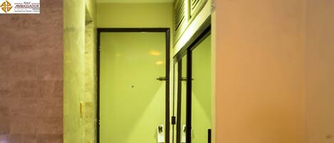 Um corredor estreito com uma porta verde, chão ladrilhado e uma parede com textura.