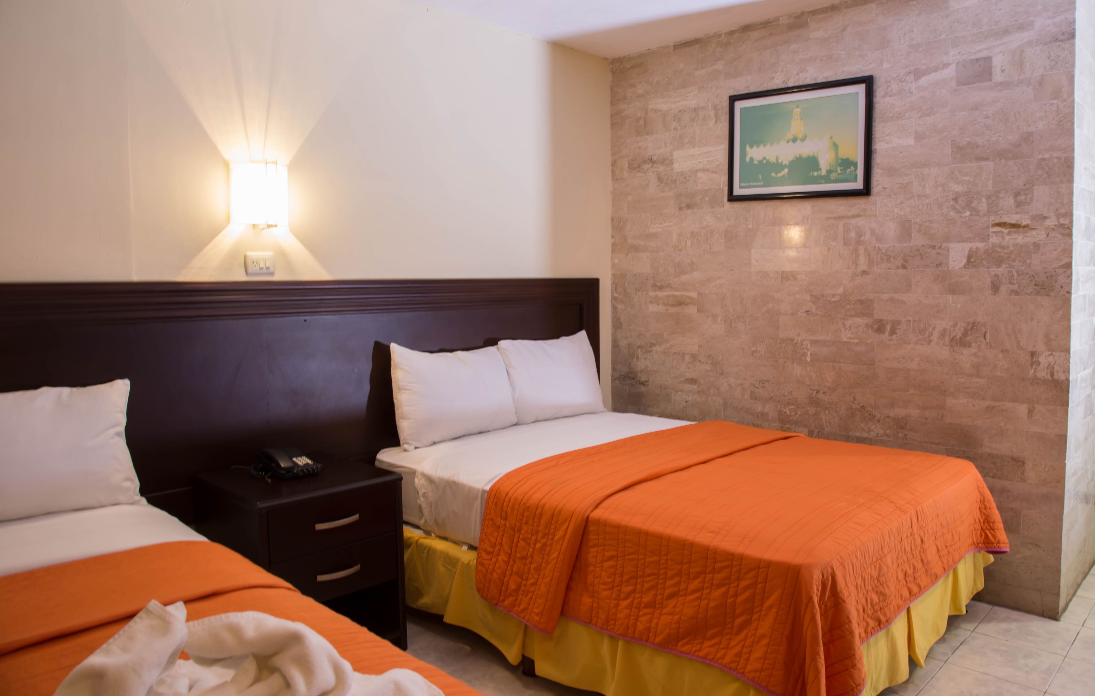 A hotel room with two beds, a nightstand, a phone, and a wall-mounted light.