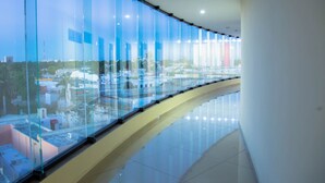 A corridor with reflective glass walls and a polished floor, leading to a high-rise building with a view of the cityscape.