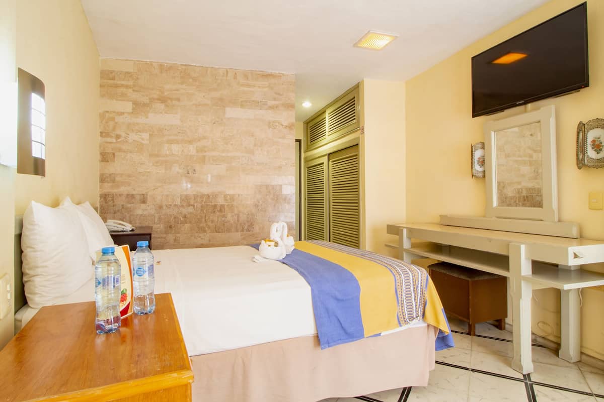 A hotel room with a bed, a desk, a television, and a bathroom with a shower.