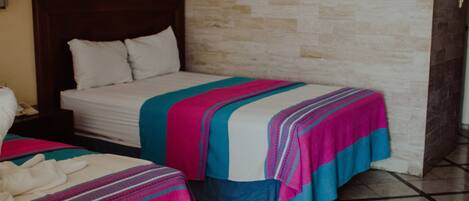 Habitación de hotel con dos camas, cada una con un edredón de estampado diferente. La habitación tiene una pared de piedra y suelo de baldosas.