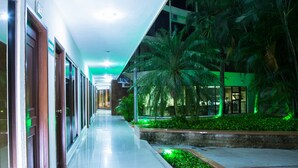 A corridor with a reflective floor, palm trees, and a building with glass doors.
