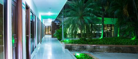 A corridor with a reflective floor, palm trees, and a building with glass doors.