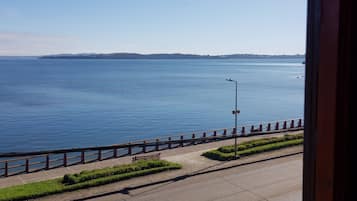 Uma estrada costeira com guarda-corpo, poste de luz e um banco.
