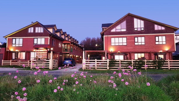 A two-story hotel with a red facade, multiple windows, and a wooden fence in front. - Hostal Vista al Mar (Ancud)