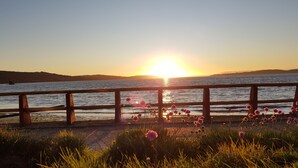 A sunset over a body of water with a wooden railing and flowers in the foreground. - Hostal Vista al Mar (Ancud)