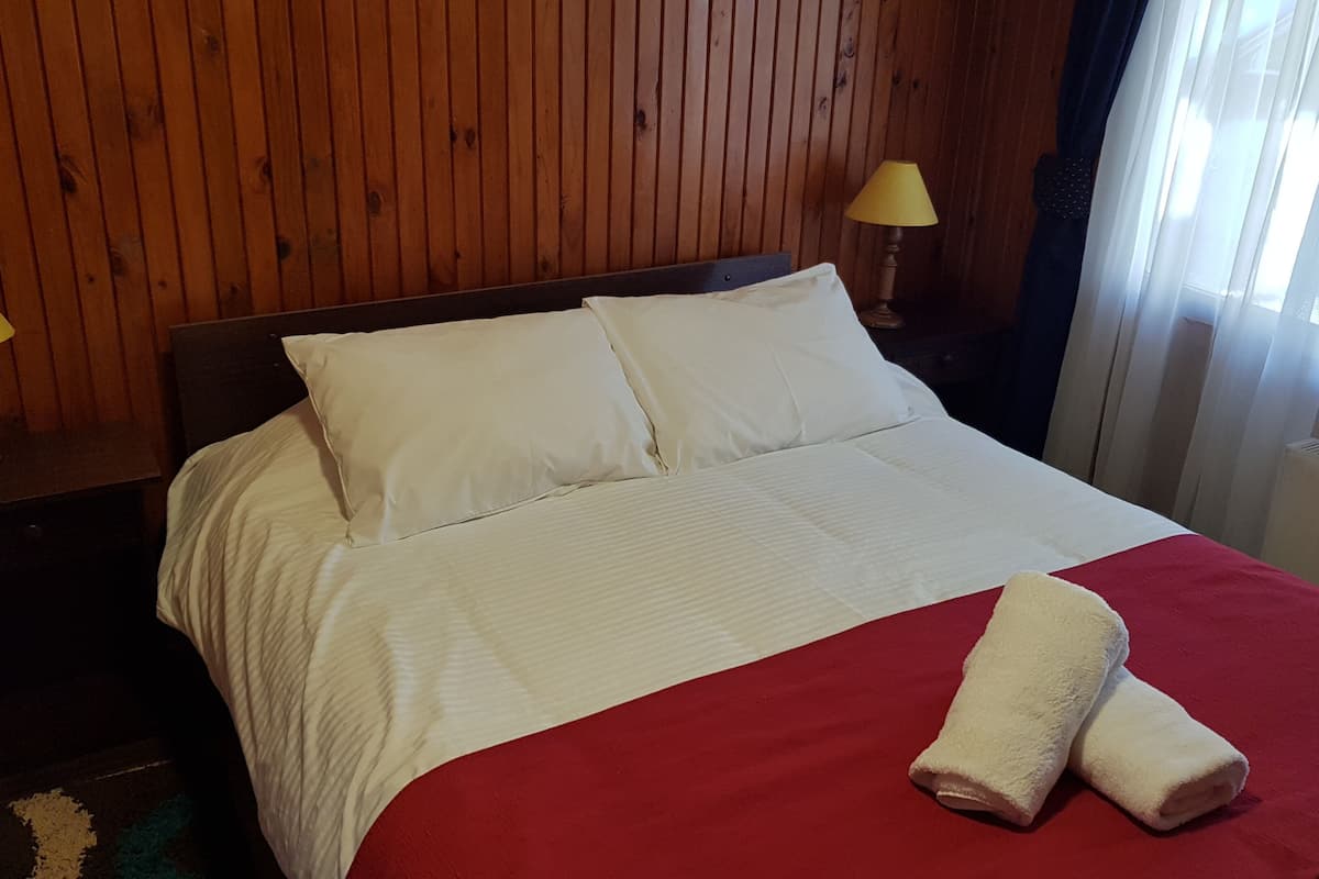 A neatly made bed with white linens and a red blanket, two bedside lamps, and wooden paneling on the walls.