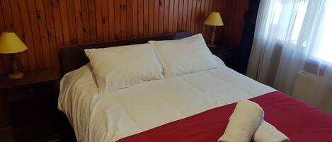 A neatly made bed with white linens and a red blanket, two bedside lamps, and wooden paneling on the walls.