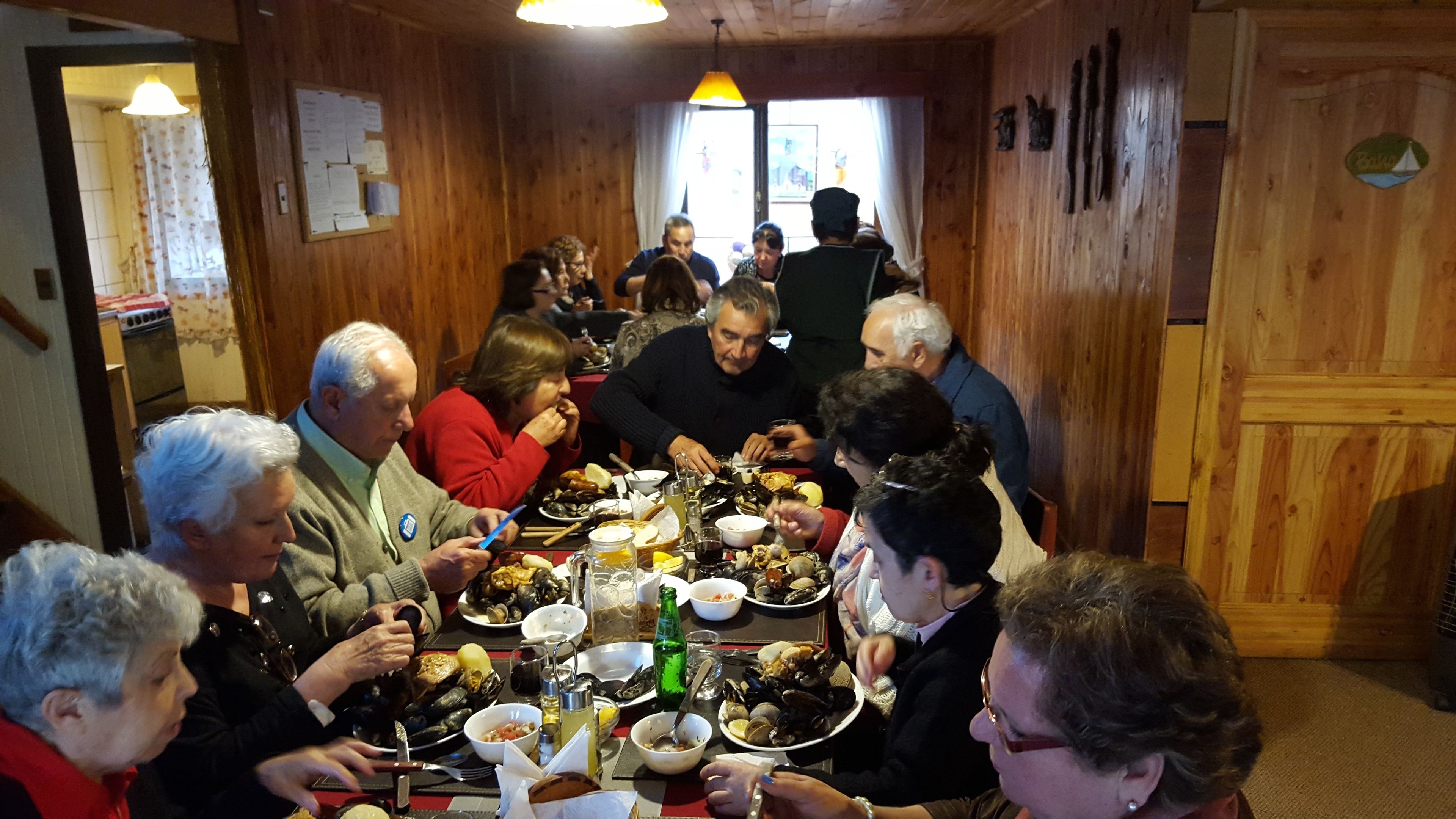 A group of people dining at a wooden table with various dishes, including seafood.