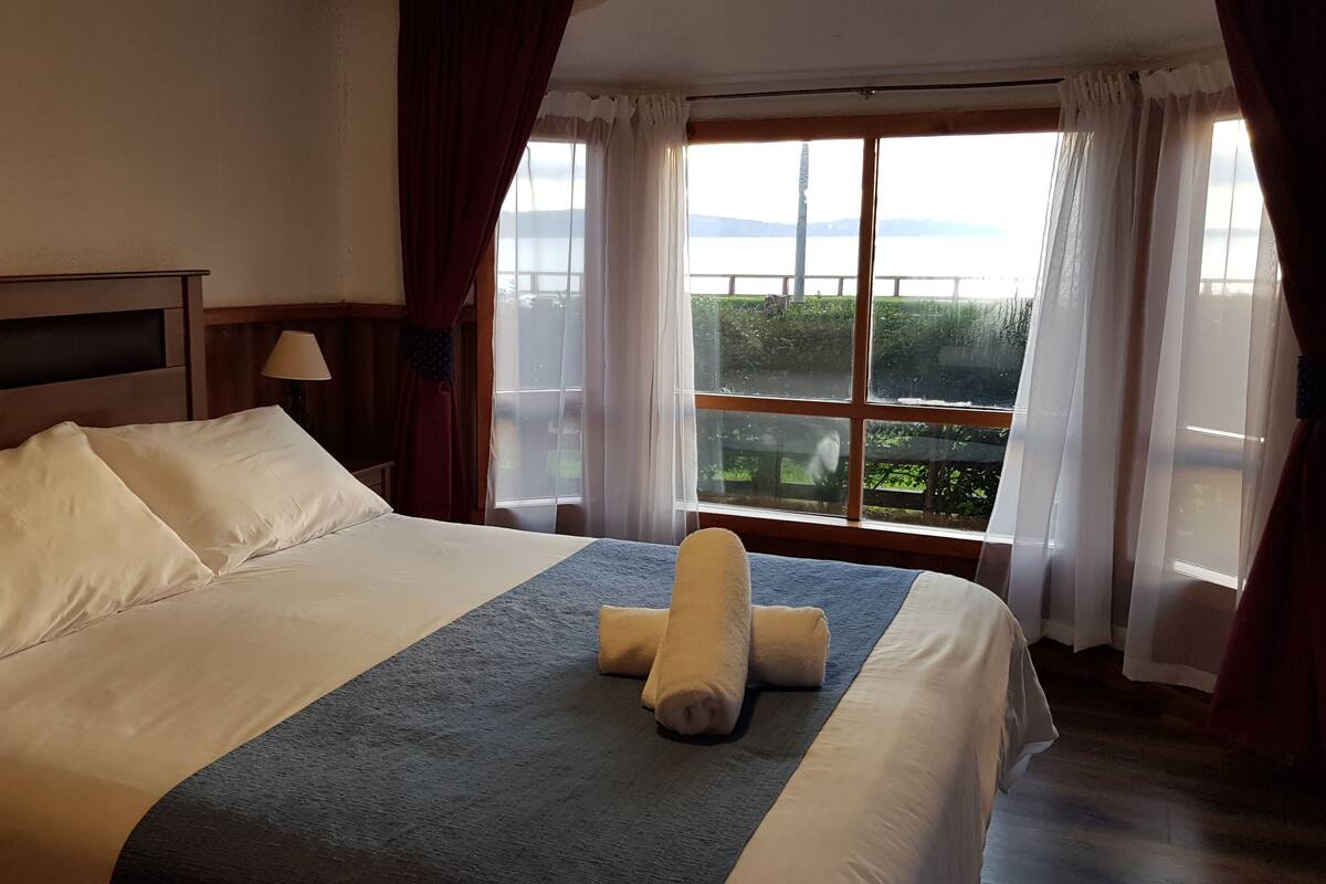 A hotel room with a large bed, a view of a lake, and a painting on the wall.