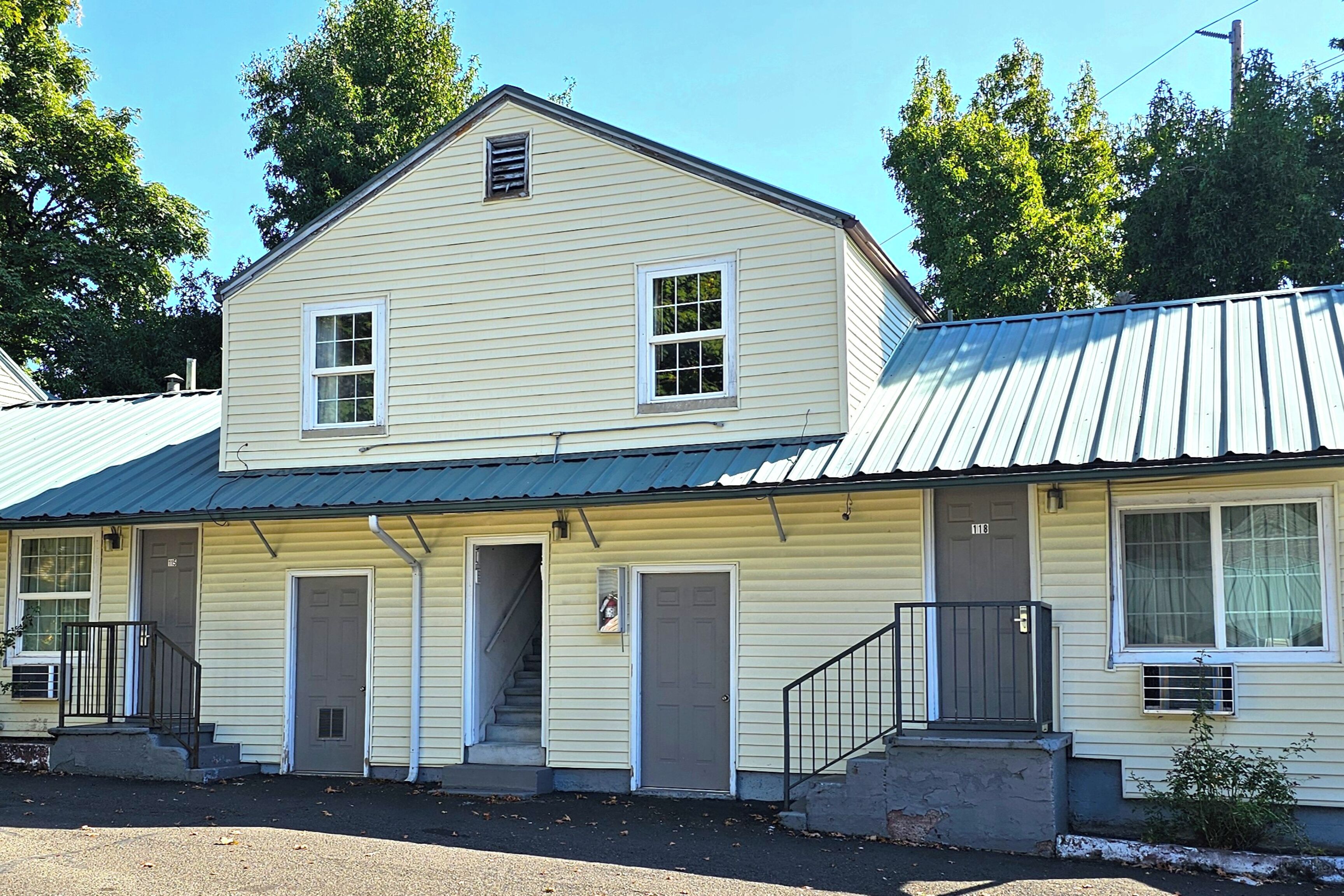 A two-story building with a metal roof, multiple doors, and a staircase leading to the entrance.
