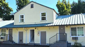 A two-story building with a metal roof, multiple doors, and a staircase leading to the entrance.