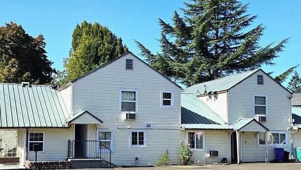 A row of two-story buildings with a metal roof, a small porch, and a visible garage door. - Budget Lodge by OYO Portland West (Portland)