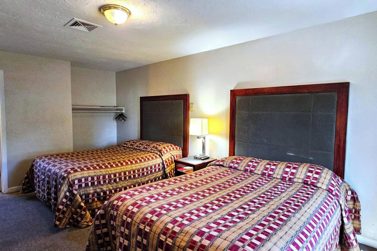 A hotel room with two beds, a nightstand, a lamp, and a large window.